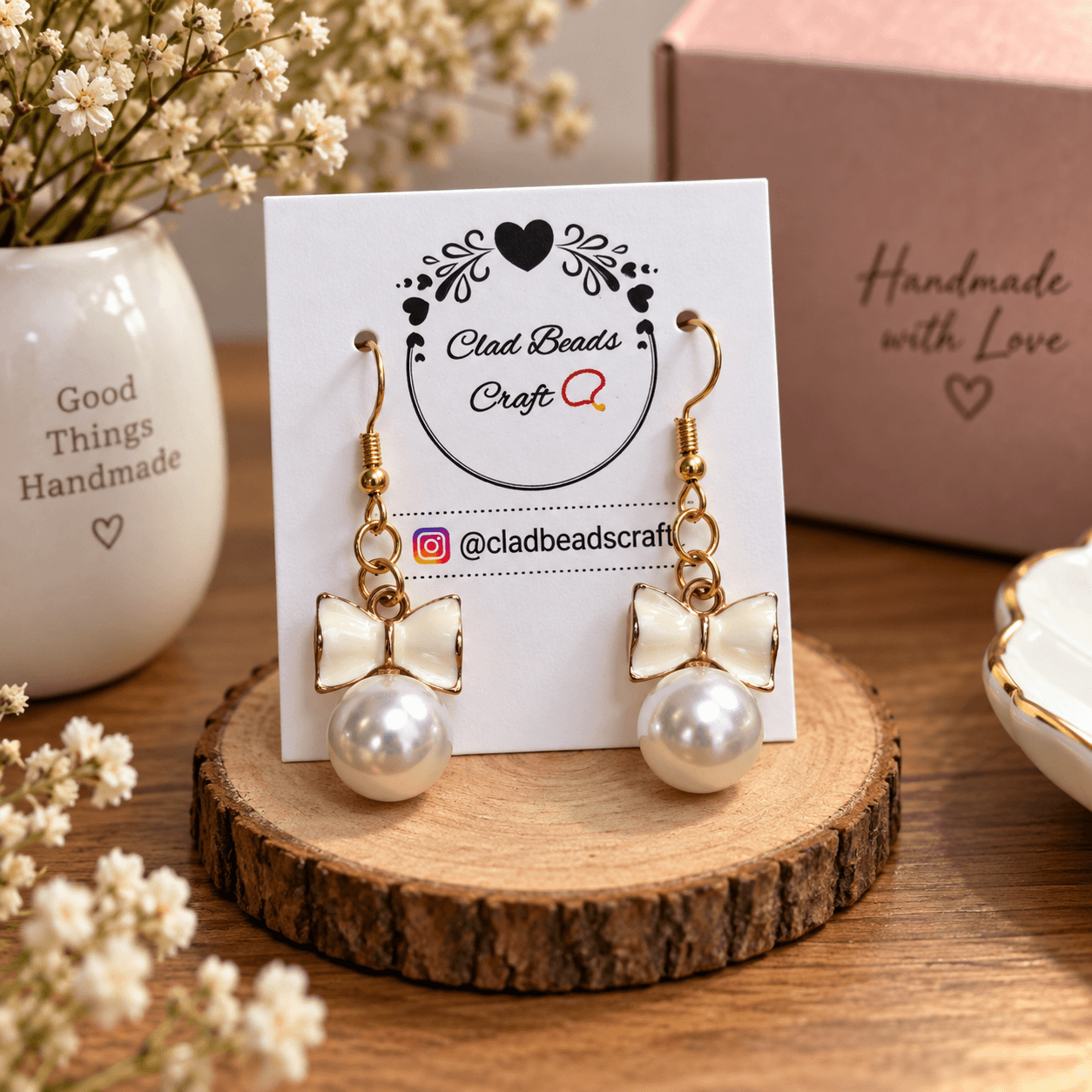 Pair of white bow pearl-look dangle earrings displayed on a Clad Beads Craft jewellery card