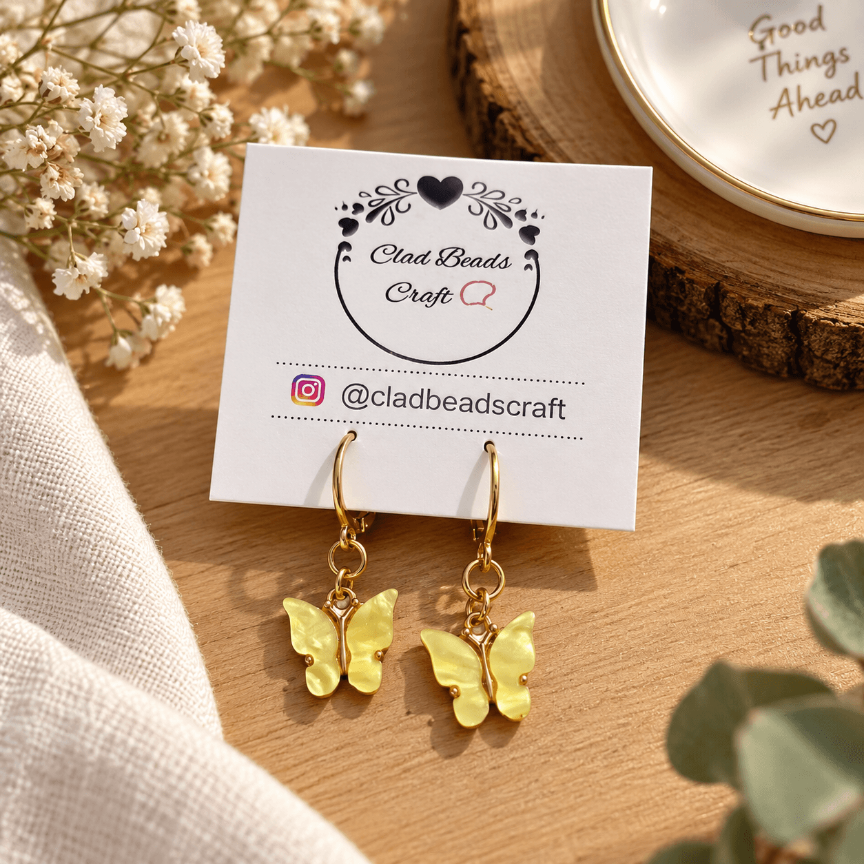 Pair of yellow butterfly dangle earrings with gold-plated hoops displayed on a Clad Beads Craft card