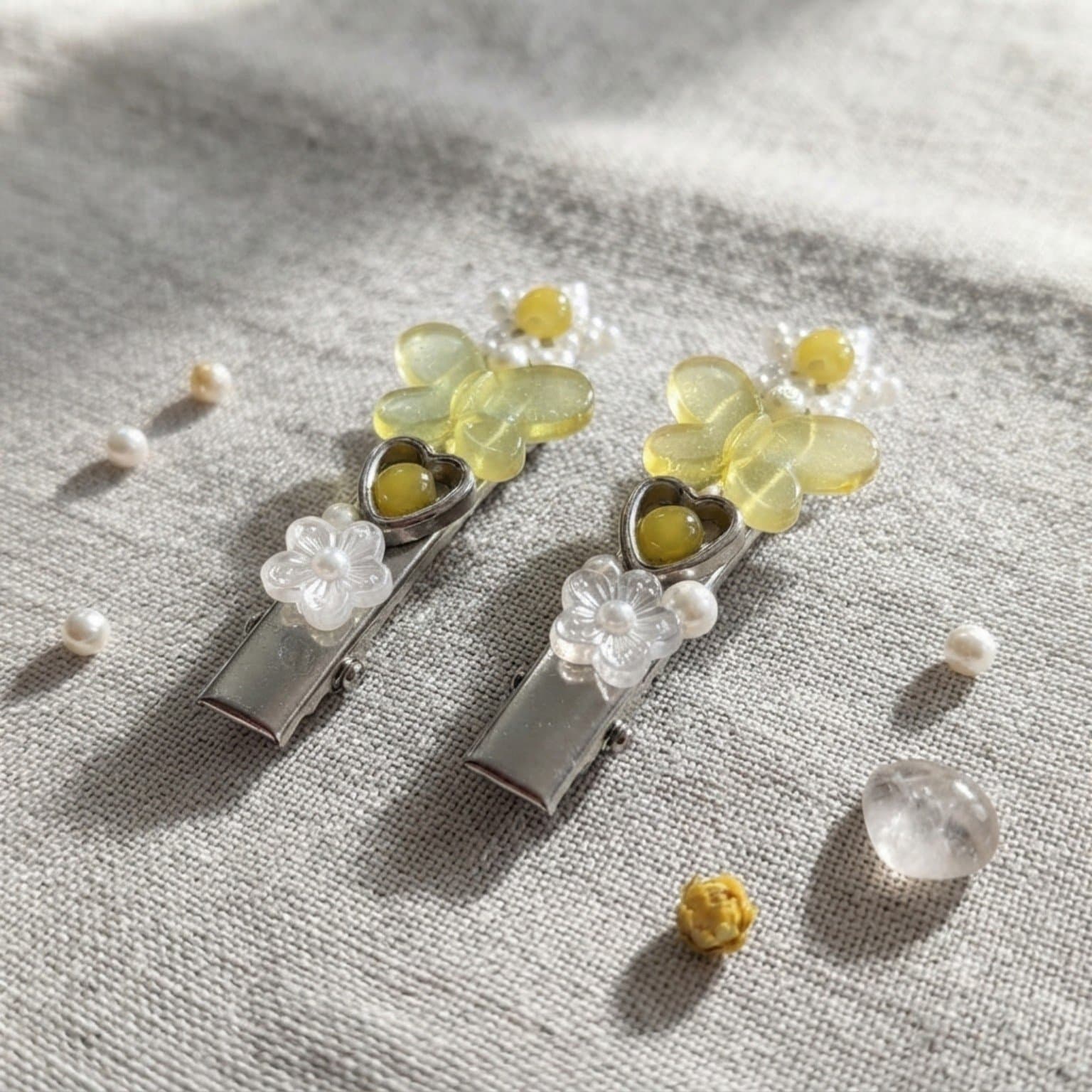 Two yellow butterfly and floral beaded hair clips displayed on a soft fabric surface