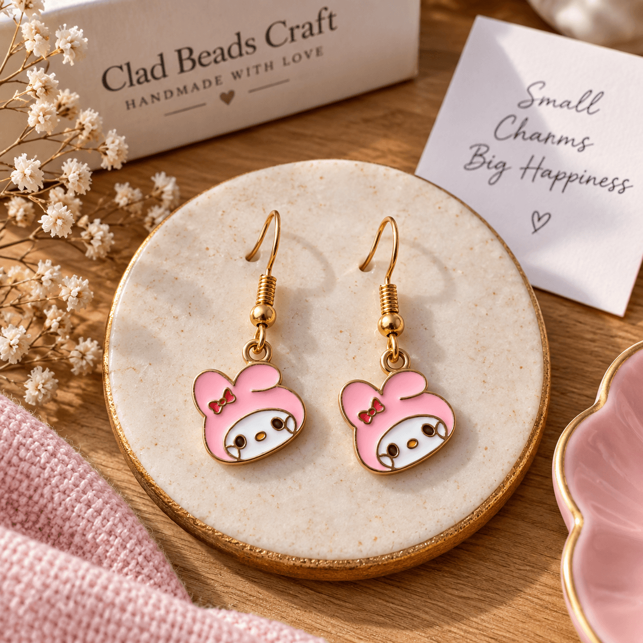 Pair of pink bunny-inspired drop earrings with white, brown and yellow details on a cream jewellery plate